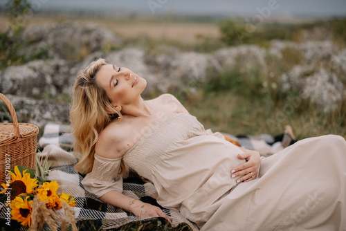 A happy pregnant blonde woman lies on the background of a mountain landscape. The concept of motherhood.