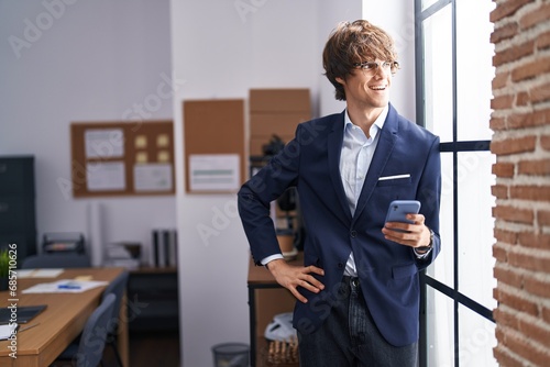 Young blond man business worker smiling confident using smartphone at office