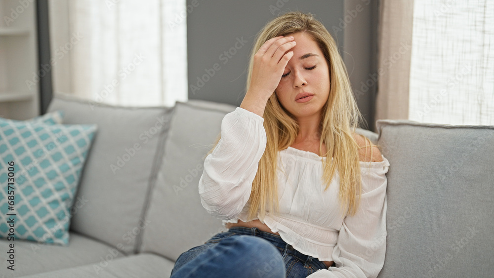 Young blonde woman suffering for headache sitting on sofa at home Young blonde woman suffering for headache sitting on sofa at home