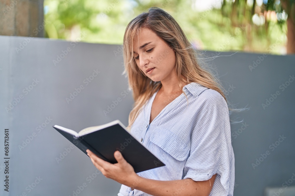Young blonde woman reading book at street