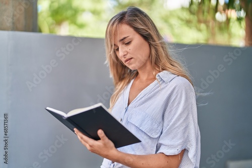 Young blonde woman reading book at street