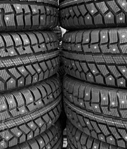 Winter studded tire. Winter car tires background. Tire stack background. Tyre protector close up. Square powerful spikes. Black studdable winter tyre profile. Car tires in a row