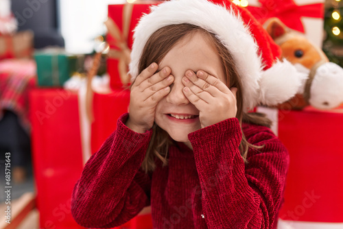 Adorable hispanic girl sitting on floor by christmas tree with eyes closed at home