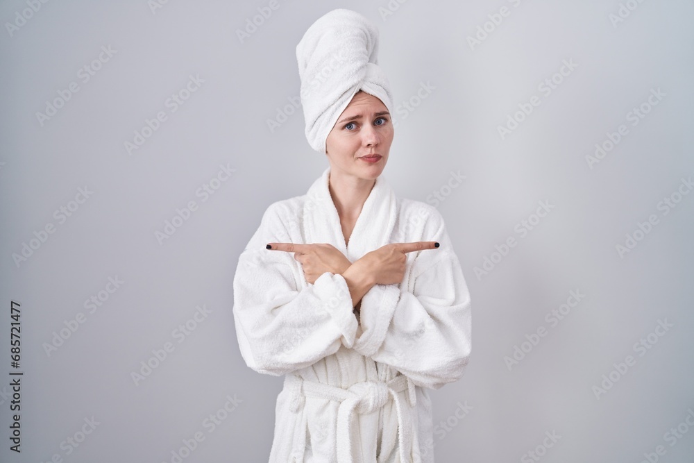 Blonde caucasian woman wearing bathrobe pointing to both sides with fingers, different direction disagree Blonde caucasian woman wearing bathrobe pointing to both sides with fingers, different direction disagree