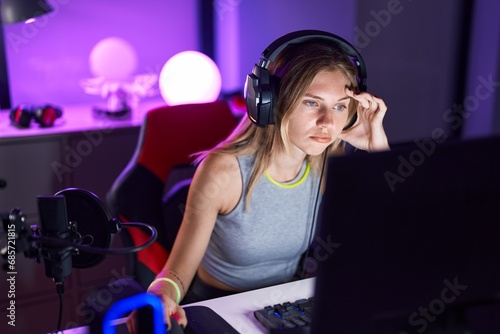 Young blonde woman streamer playing video game using computer tired at gaming room