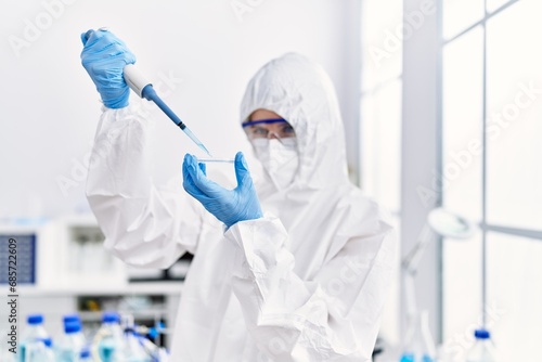 Young blonde woman scientist wearing security uniform pouring liquid on sample at laboratory