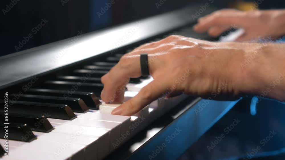 The young musician's hands play the piano in a dark studio with a light at the back. The young musician's hands play the piano in a dark studio with a light at the back.