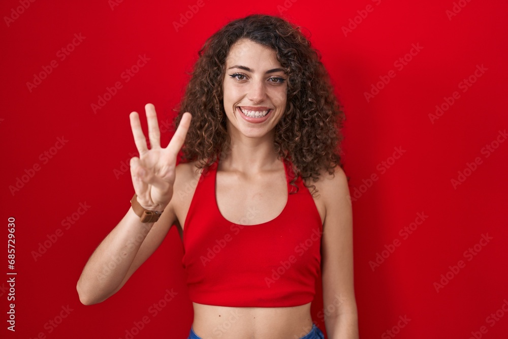 Hispanic woman with curly hair standing over red background showing and pointing up with fingers number three while smiling confident and happy. Hispanic woman with curly hair standing over red background showing and pointing up with fingers number three while smiling confident and happy.