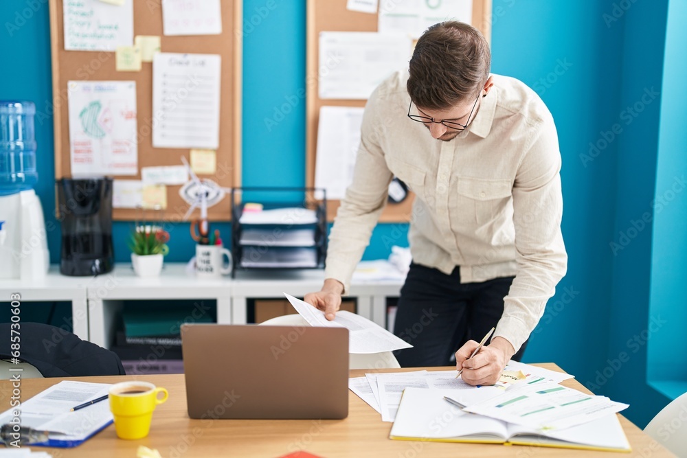 Young caucasian man business worker using laptop writing on document at office