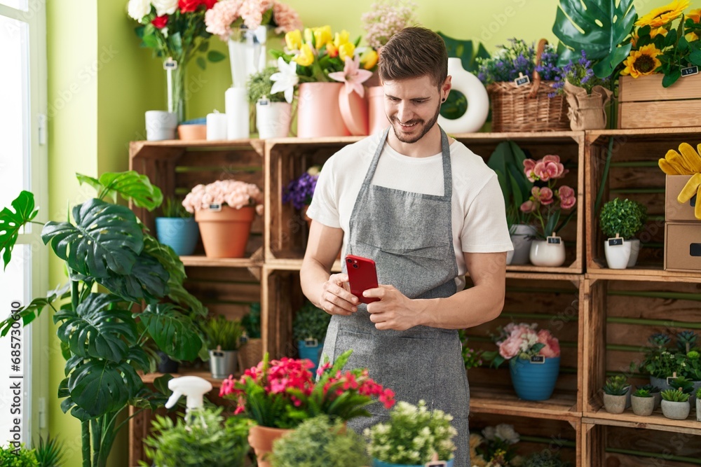 Young caucasian man florist make photo to flowers by smartphone at flower shop