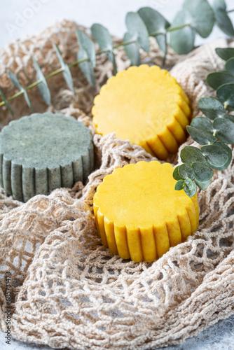 Eco-friendly solid handmade bright green and yellow shampoo bars on mesh bag background