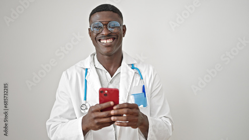 African american man doctor smiling using smartphone over isolated white background