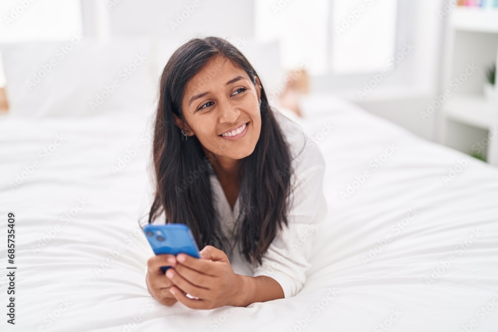 Young beautiful hispanic woman using smartphone lying on bed at bedroom Young beautiful hispanic woman using smartphone lying on bed at bedroom