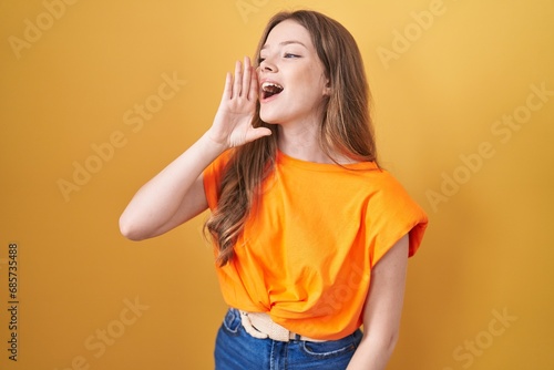 Caucasian woman standing over yellow background shouting and screaming loud to side with hand on mouth. communication concept.
