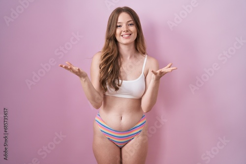 Caucasian woman wearing lingerie over pink background smiling cheerful offering hands giving assistance and acceptance. © Krakenimages.com
