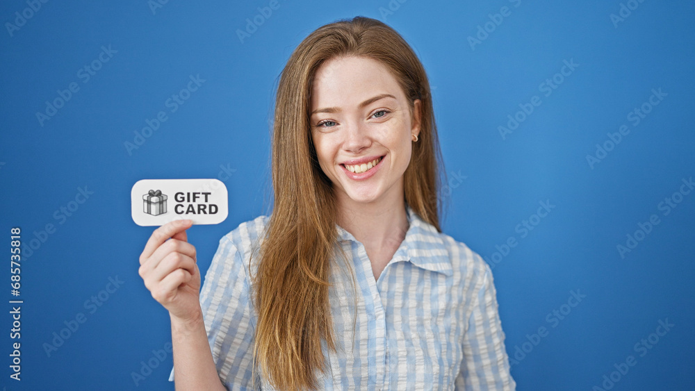 Young blonde woman smiling confident holding gift card over isolated blue background Young blonde woman smiling confident holding gift card over isolated blue background