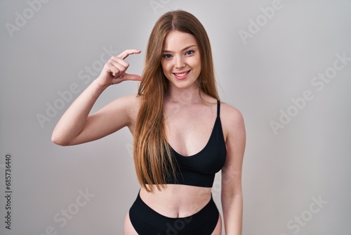 Young caucasian woman wearing lingerie smiling and confident gesturing with hand doing small size sign with fingers looking and the camera. measure concept.