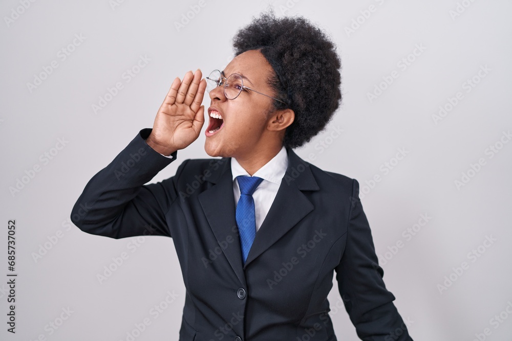 Beautiful african woman with curly hair wearing business jacket and glasses shouting and screaming loud to side with hand on mouth. communication concept. Beautiful african woman with curly hair wearing business jacket and glasses shouting and screaming loud to side with hand on mouth. communication concept.