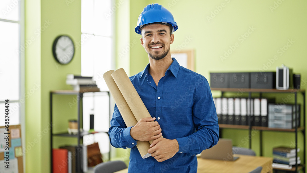 Young hispanic man architect wearing hardhat holding blueprints at office Young hispanic man architect wearing hardhat holding blueprints at office