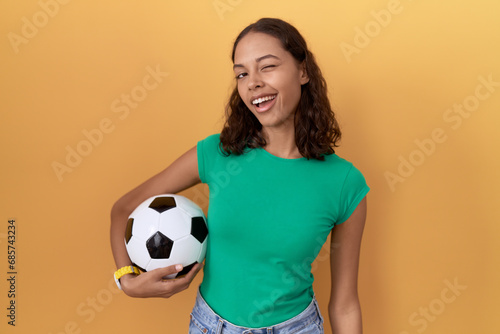 Young hispanic woman holding ball winking looking at the camera with sexy expression, cheerful and happy face. © Krakenimages.com