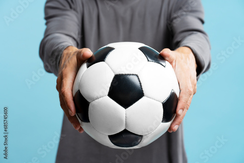 Closeup man hands holding soccer ball isolated on blue background, selective focus. Sport, football, competition concept  © Maria Vitkovska