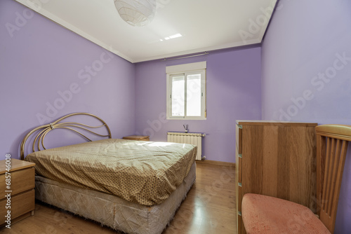 A room with a double bed with an old folding sofa  a gold metal headboard and walls painted a soft purple