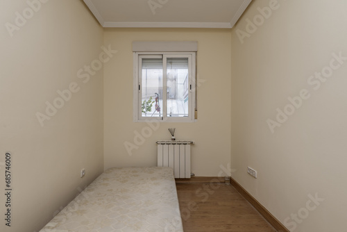 A small empty room with an old folding sofa and a white aluminum radiator under the window made of the same material