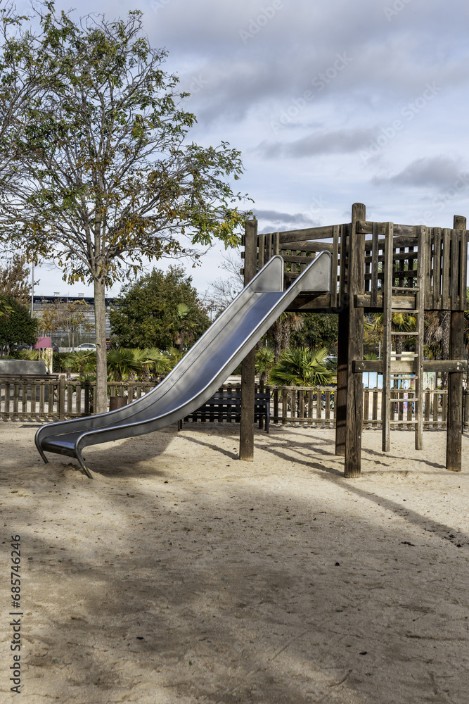 A metal slide with an unvarnished wooden structure in a municipal urban park