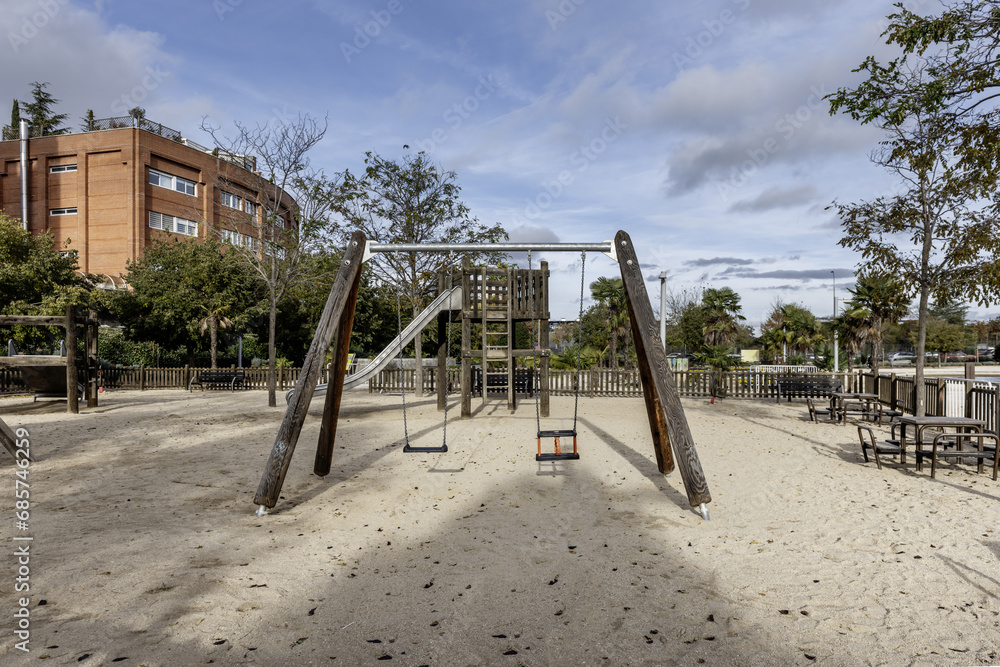 Some swings with an unvarnished wooden structure in a municipal urban park