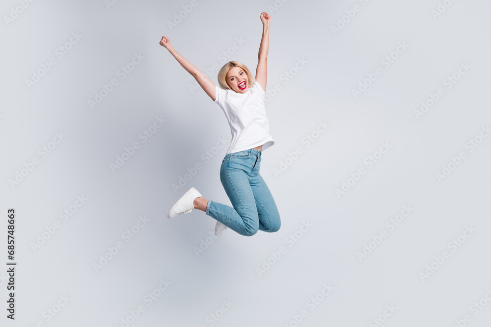 Full size photo of overjoyed woman dressed white t-shirt denim pants flying win lottery raisng fists up isolated on white color background