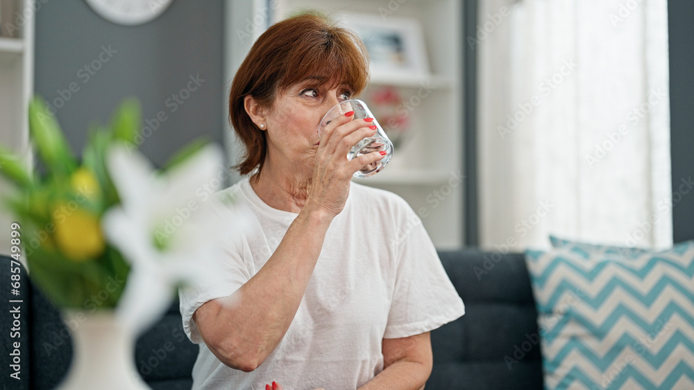 Middle age woman drinking glass of water sitting on sofa home Middle age woman drinking glass of water sitting on sofa home