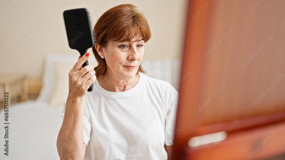 Middle age woman combing hair looking on mirror at bedroom Middle age woman combing hair looking on mirror at bedroom