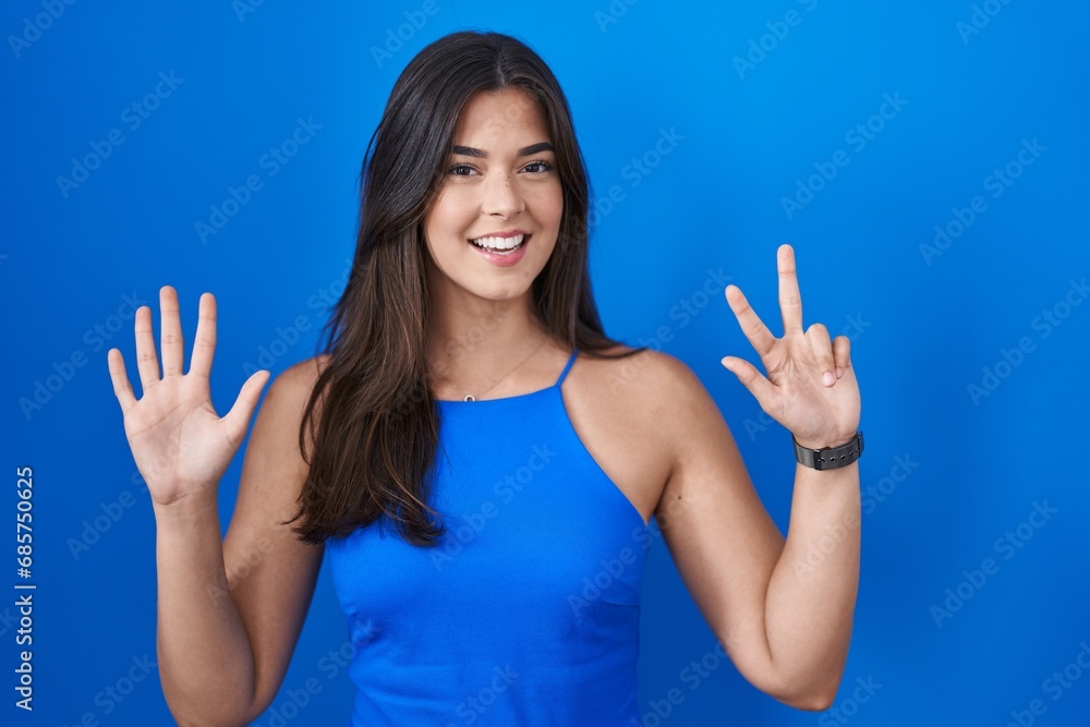 Hispanic woman standing over blue background showing and pointing up with fingers number eight while smiling confident and happy. Hispanic woman standing over blue background showing and pointing up with fingers number eight while smiling confident and happy.