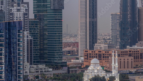 New white mosque near bay avenue surrounded by skyscrapers in Business Bay district aerial day to night timelapse. photo