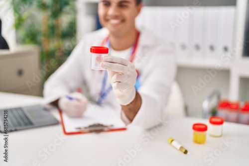 Young hispanic man doctor writing medical report holding urine test tube at clinic