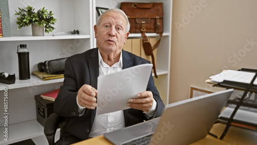 Serious, mature gentleman hard at work, elegant white-haired senior man, a seasoned business professional, engrossed in documents while speaking earnestly at the office.