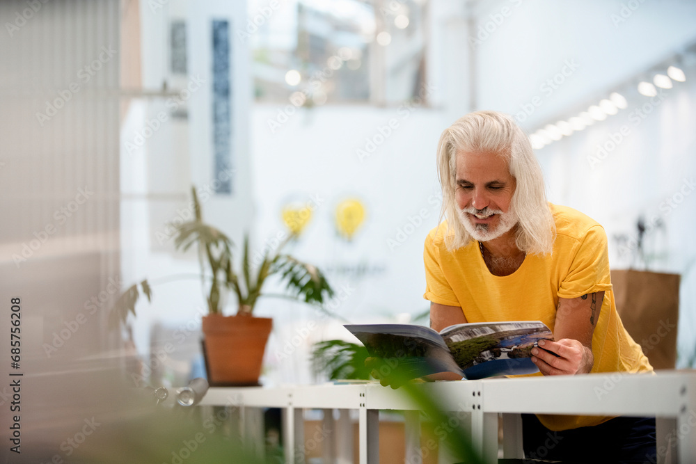 Adult male designer leaning on table while reading magazine Adult male designer leaning on table while reading magazine