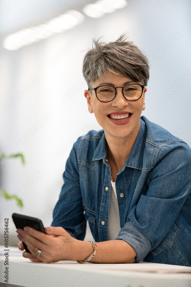 Female designer using smart phone while looking at the camera Female designer using smart phone while looking at the camera