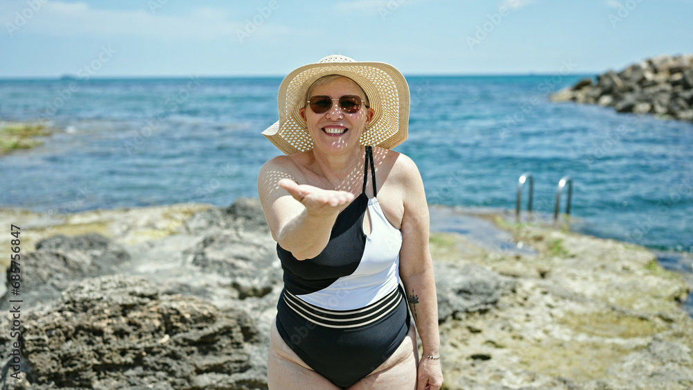 Middle age grey-haired woman tourist wearing swimsuit and summer hat blowing kiss at the beach Middle age grey-haired woman tourist wearing swimsuit and summer hat blowing kiss at the beach