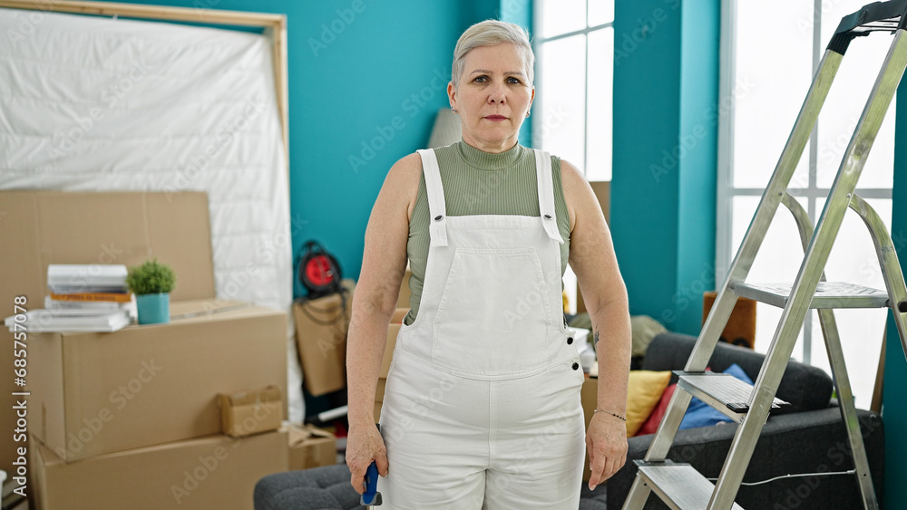 Obraz premium Middle age grey-haired woman standing with serious face at new home