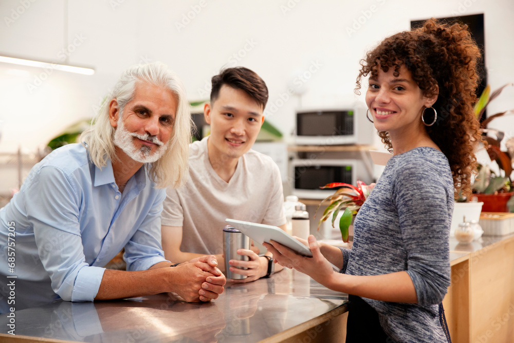 Fototapeta premium Coworkers looking at the camera while holding digital tablet at office kitchen