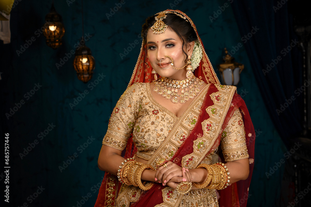 Stunning Indian bride dressed in traditional bridal lehenga with heavy gold jewellery and veil posing fashionable in studio lighting. Wedding fashion and lifestyle.