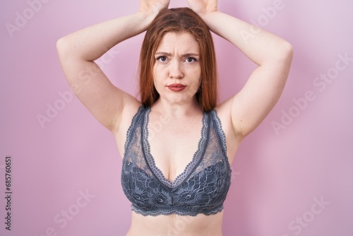 Redhead woman wearing lingerie over pink background doing bunny ears gesture with hands palms looking cynical and skeptical. easter rabbit concept. photo