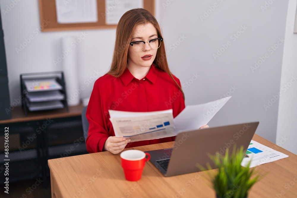 Young redhead woman business worker using laptop reading document at office Young redhead woman business worker using laptop reading document at office
