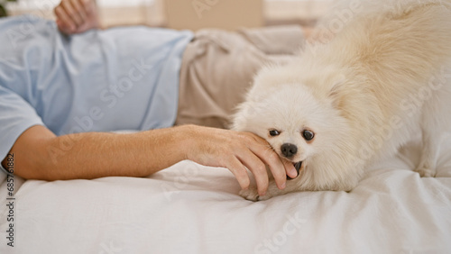 Fototapeta Naklejka Na Ścianę i Meble -  Relaxed morning scenario with handsome young caucasian man, effortlessly chilling with his loyal dog lying on the comfortable bed in bedroom. loving the expressively playful, indoor lifestyle.