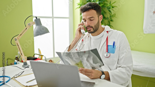 Young hispanic man doctor talking on telephone holding xray at clinic