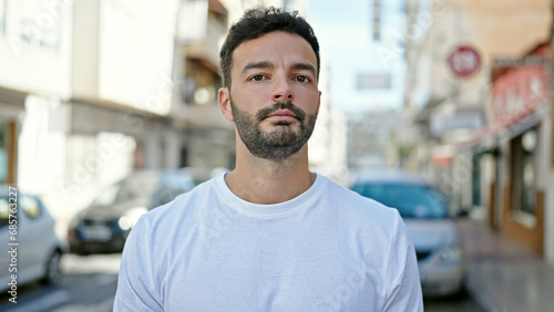 Young hispanic man standing with serious expression at street
