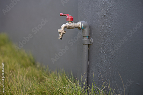 The faucet is installed on the fence wall near the lawn. photo