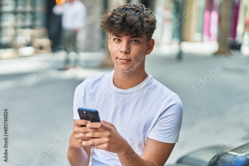 Young hispanic teenager using smartphone with relaxed expression at street