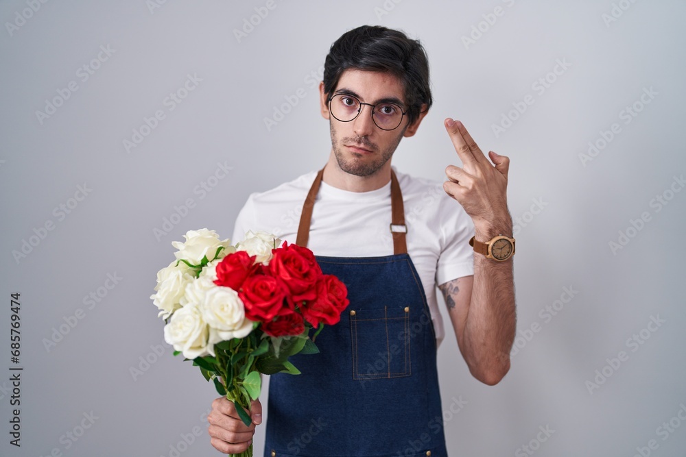 Young hispanic man holding bouquet of white and red roses shooting and killing oneself pointing hand and fingers to head like gun, suicide gesture. Young hispanic man holding bouquet of white and red roses shooting and killing oneself pointing hand and fingers to head like gun, suicide gesture.